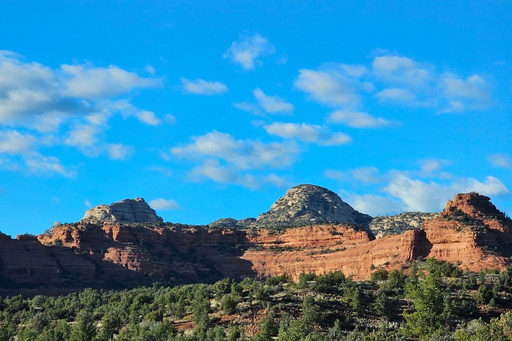 Red sandstone buttes under a deep blue sky with a road curving through green desert scrub in the foreground