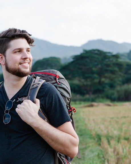 Portrait of a person with a large trekking pack standing in a field with hills behind