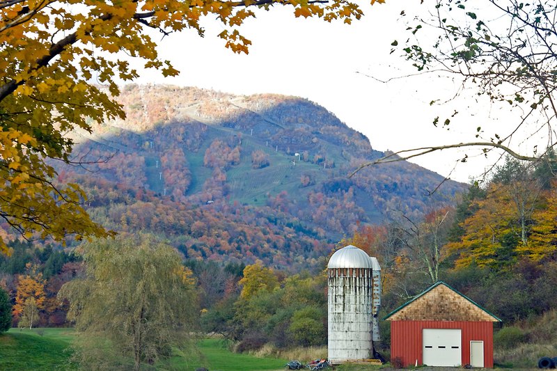 A red barn and a white silo in a field with fall hills and a mountain behind