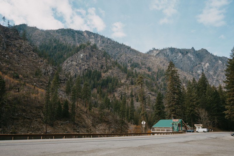 A small roadside diner with a green roof below steep forested mountains in Washington