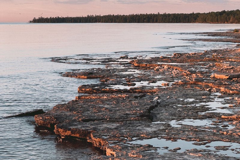 A rocky lakeshore at sunset with pink light on the water in Wisconsin
